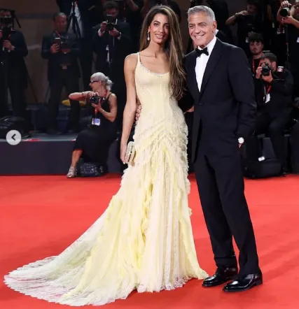 Amal Clooney in a Giambattista Valli gown on the red carpet, showcasing her iconic style and fashion with bouncy curls.