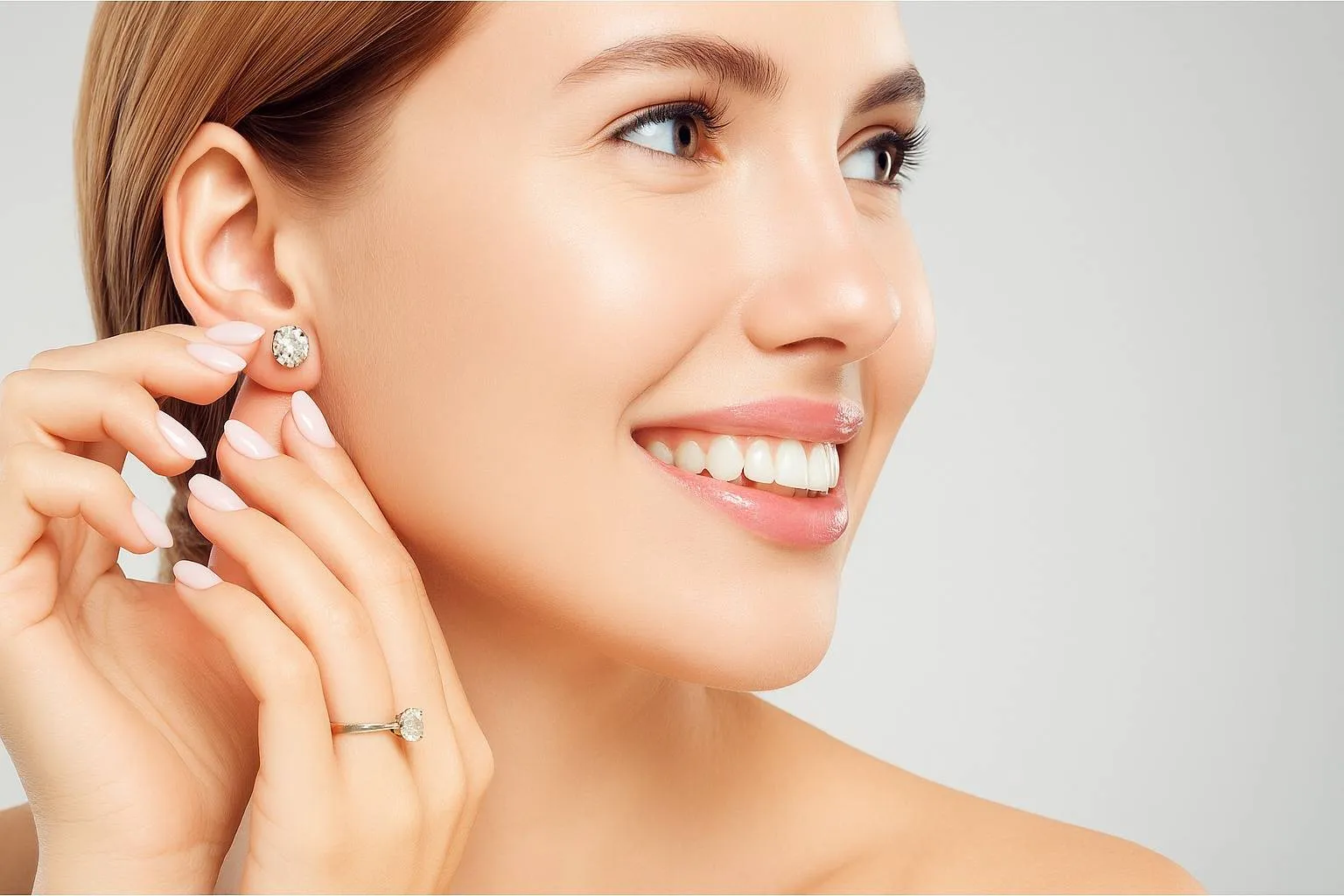 A smiling woman wearing a simple yet stunning diamond stud earring, paired with a matching ring. Her bright smile and manicured nails add to the overall polished and glamorous appearance.
