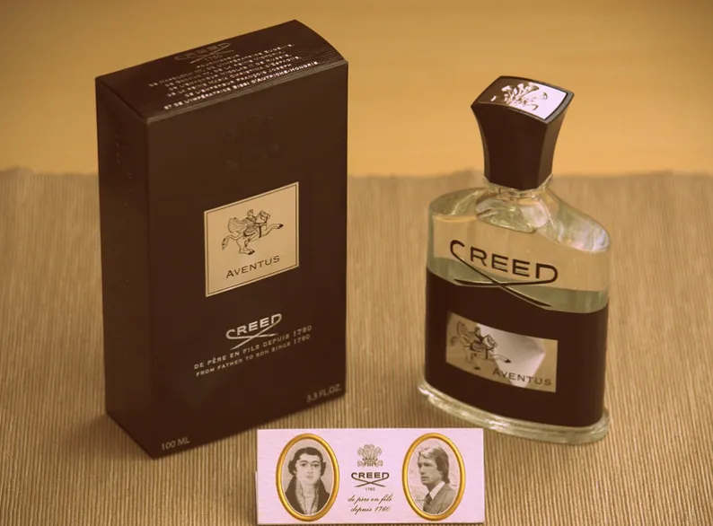 Creed Aventus cologne bottle surrounded by fresh pineapple and birchwood, representing confidence and power.